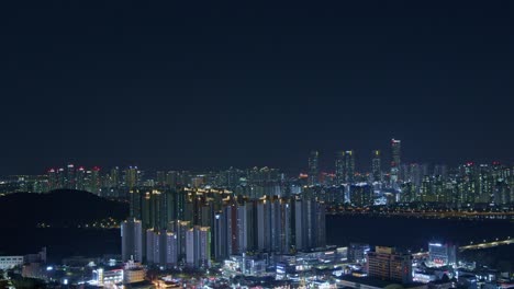 Vista-Panorámica-Urbana-De-La-Ciudad-Nocturna-Desde-Un-ángulo-Alto-Con-Construcciones,-Rascacielos-Y-Puentes