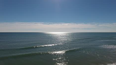 Drone-shot-moving-up-above-gentle-ocean-waves-towards-the-clear-blue-sky-on-a-sunny-day