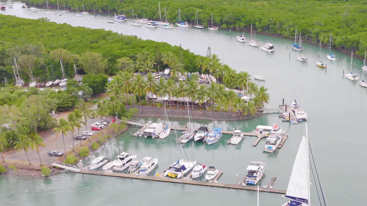 Aerial footage captures yachts docked in a lush marina surrounded by greenery in Port Douglas, Australia, under soft daylight
