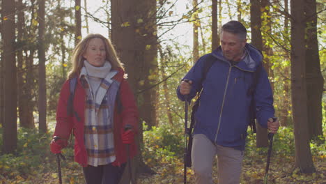 front view of mature couple walking through fall or winter countryside using hiking poles - shot in slow motion