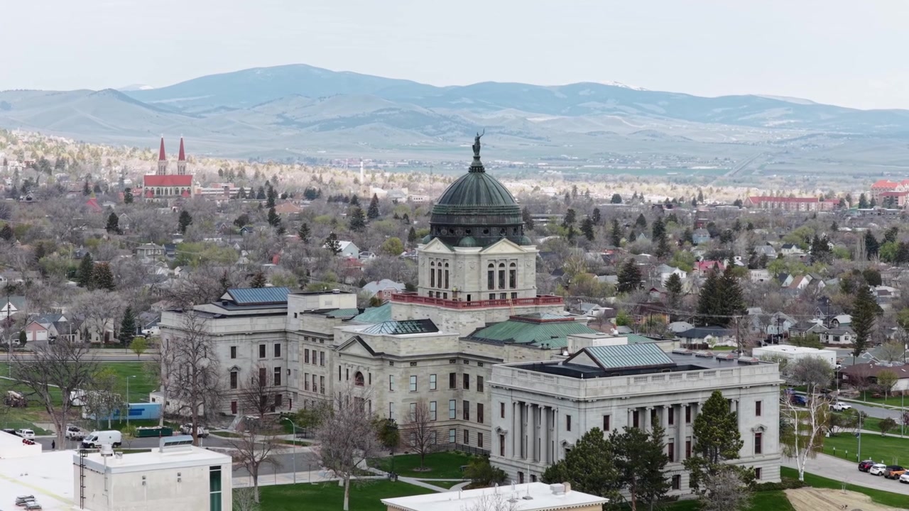 Edificio del Campidoglio dello Stato del Montana a Helena con la città circostante e montagne distanti sotto una luce diurna soffusa che mostra l'architettura governativa storica e il paesaggio regionale negli Stati Uniti. Orbita aerea