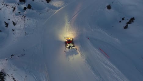 aerial drone shot of a snow groomer in action. low light end of the day.