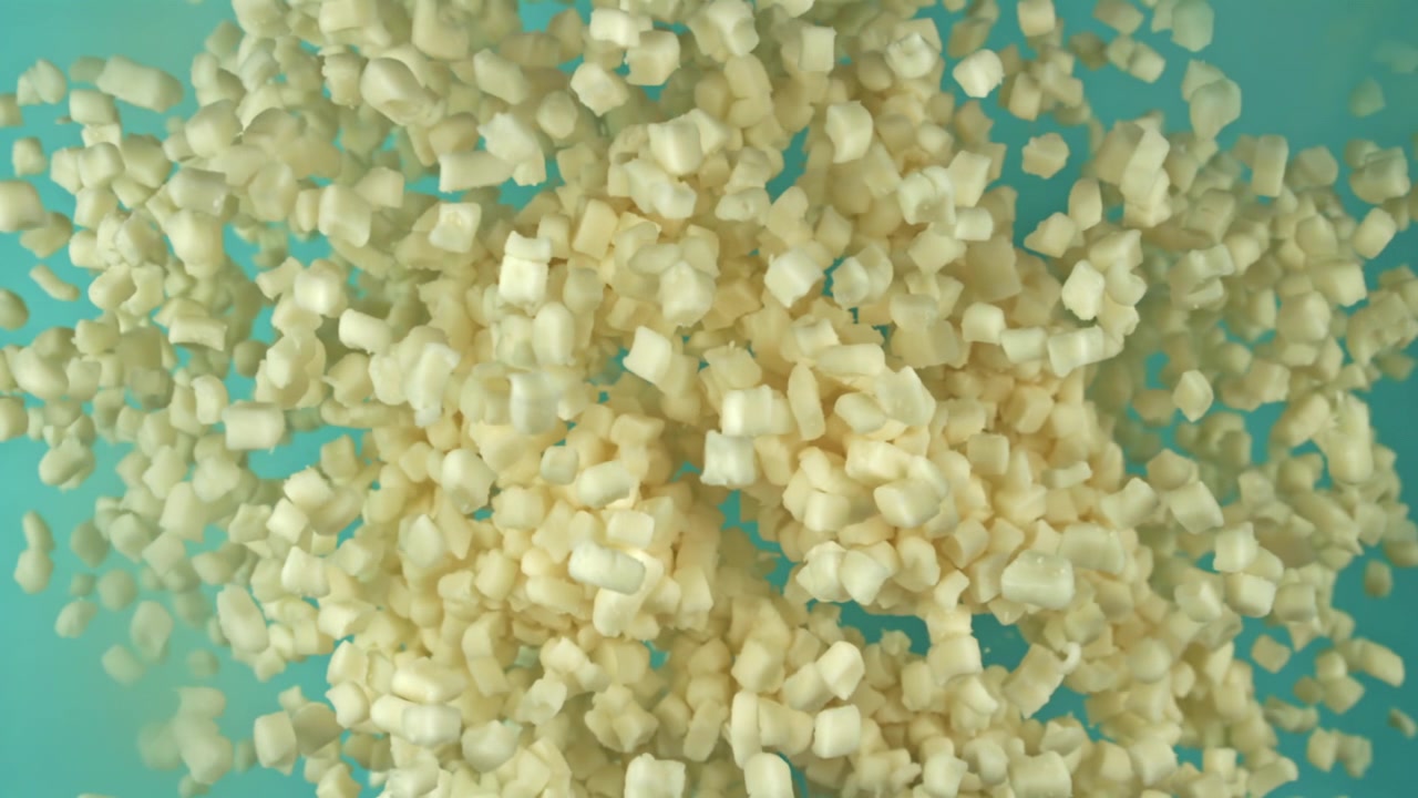 Cubetti di cibo bianchi a dadini che galleggiano in acqua turchese al rallentatore.