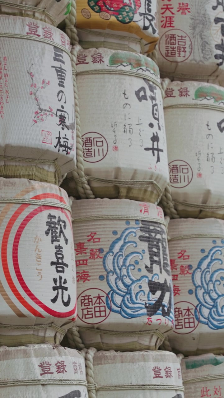 Vertical slow moving video of beautifully decorated sake barrels at Meiji Jingu Shrine during the daytime in Yoyogi Park in Tokyo.