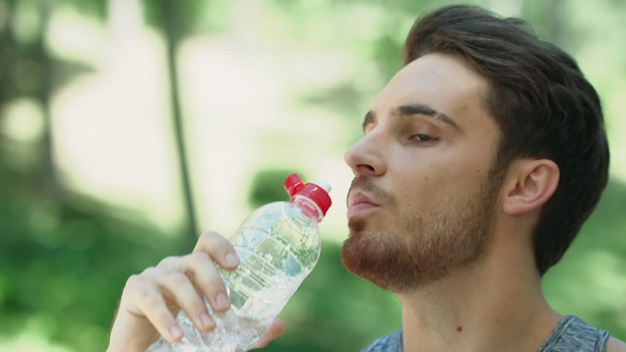 hombre sediento bebiendo agua de la botella en el parque de verano. retrato de hombre deportivo