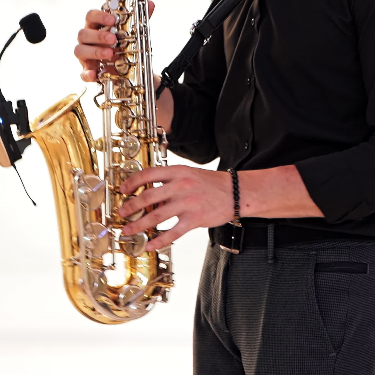 Saxophonist in black shirt and trousers plays jazz on golden saxophone with microphone. Musician male performs music on a saxophone against the blurred background. Live performance.