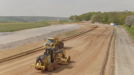 Aerial-of-a-grader-and-a-dump-truck-pass-each-other-on-a-large-construction-site