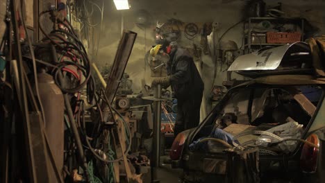 man angel grinds metal plate on steel piping in messy workshop