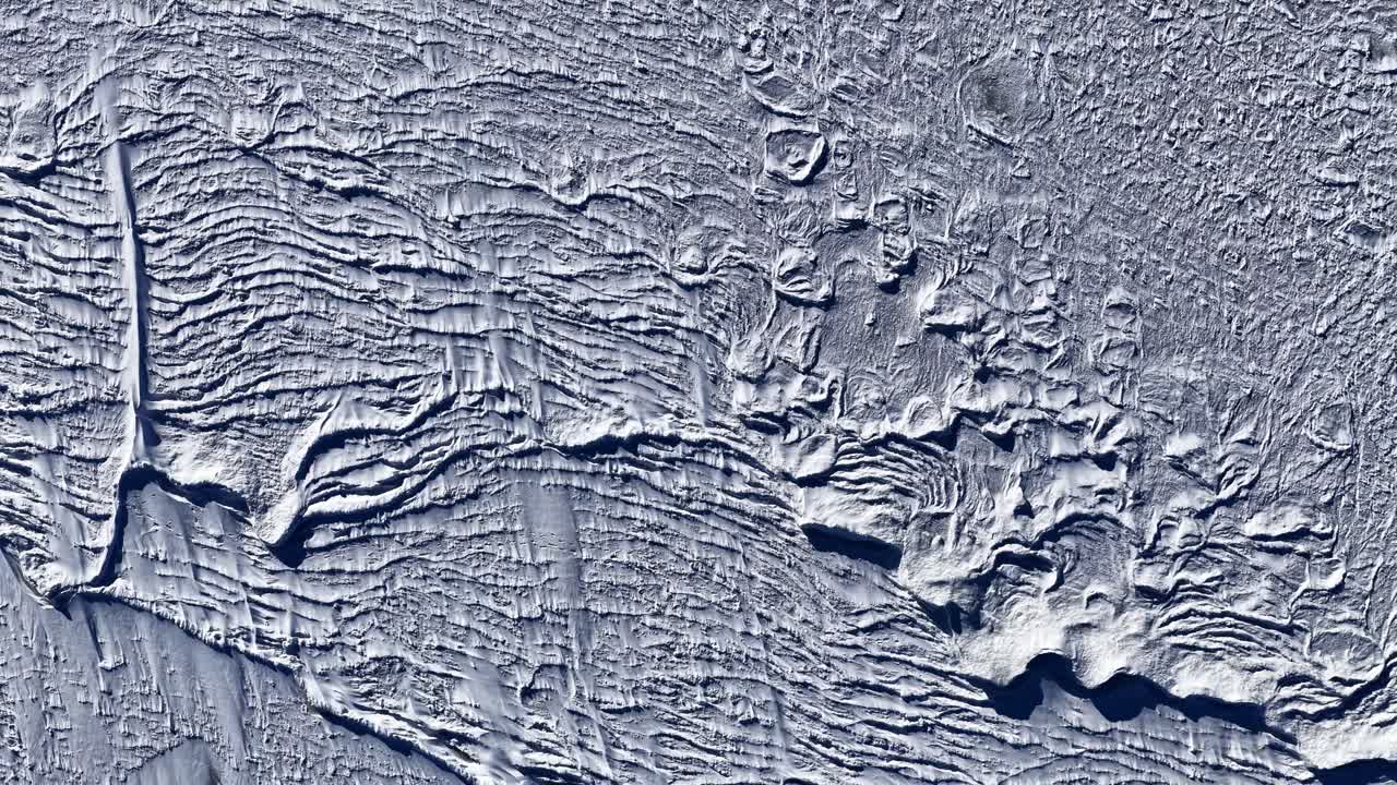 Aerial close-up of frozen sea with pressure ridges and windblown snow, creating dramatic abstract winter texture for backgrounds and climate visuals