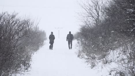 Back-of-couple-walking-their-dog-on-snowy-road-during-snow-storm