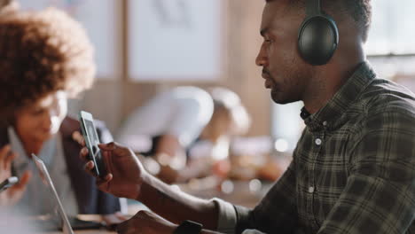 Joven-Afroamericano-Usando-Una-Computadora-Portátil-En-Una-Cafetería-Navegando-En-Línea-Revisando-Mensajes-En-Un-Teléfono-Inteligente-Escuchando-Música-Trabajando-En-Una-Cafetería