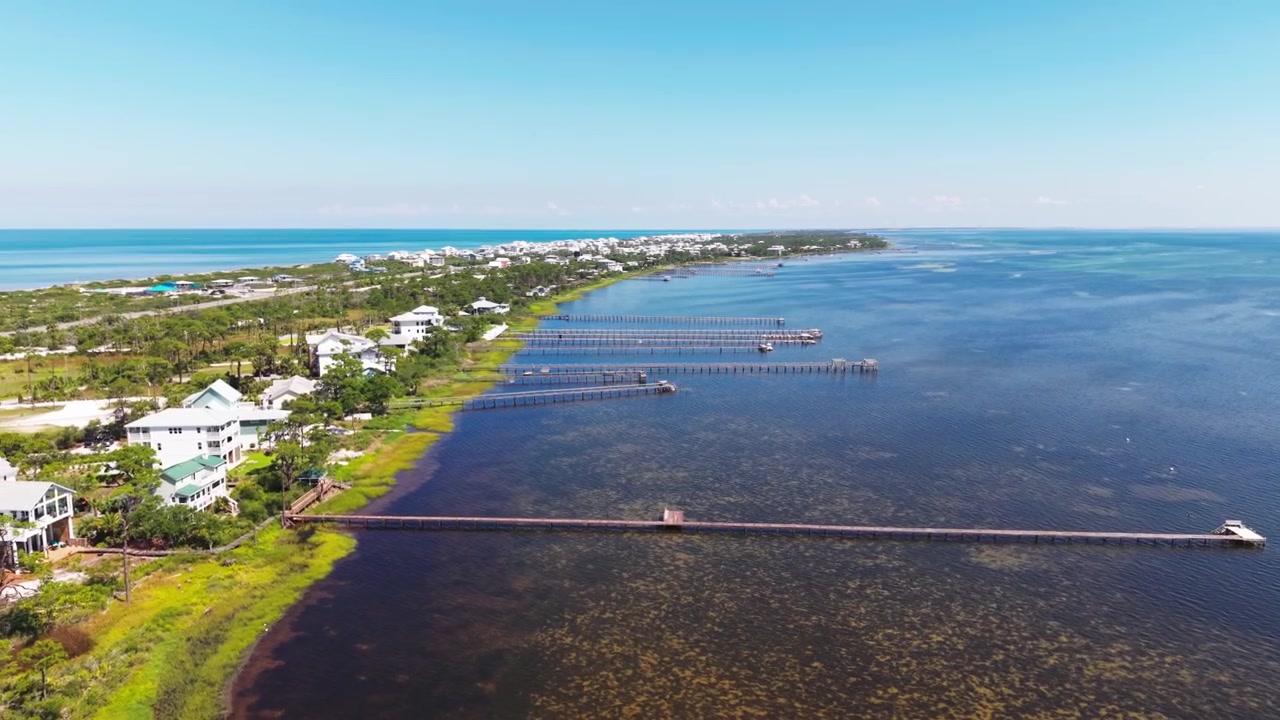 Panoramatický záběr dronem na řadu luxusních pobřežních domů s mnoha soukromými moly sahajícími daleko do mělké a mechové zátoky St. Joseph, se vzdálenou plážovou oblastí Cape San Blas, Florida, USA.