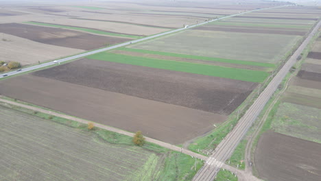 Drone-tilt-up-Aerial-rural-road-splitting-agricultural-green-and-brown-Farmland