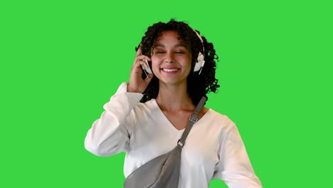 smiling young african american woman walking and listening to music on headphones on a green screen, chroma key