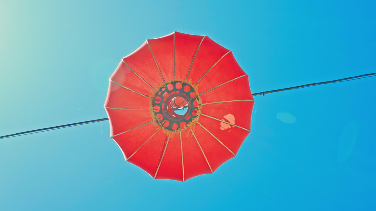 Rød kinesisk lanterne hænger mod blå himmel på en solrig dag