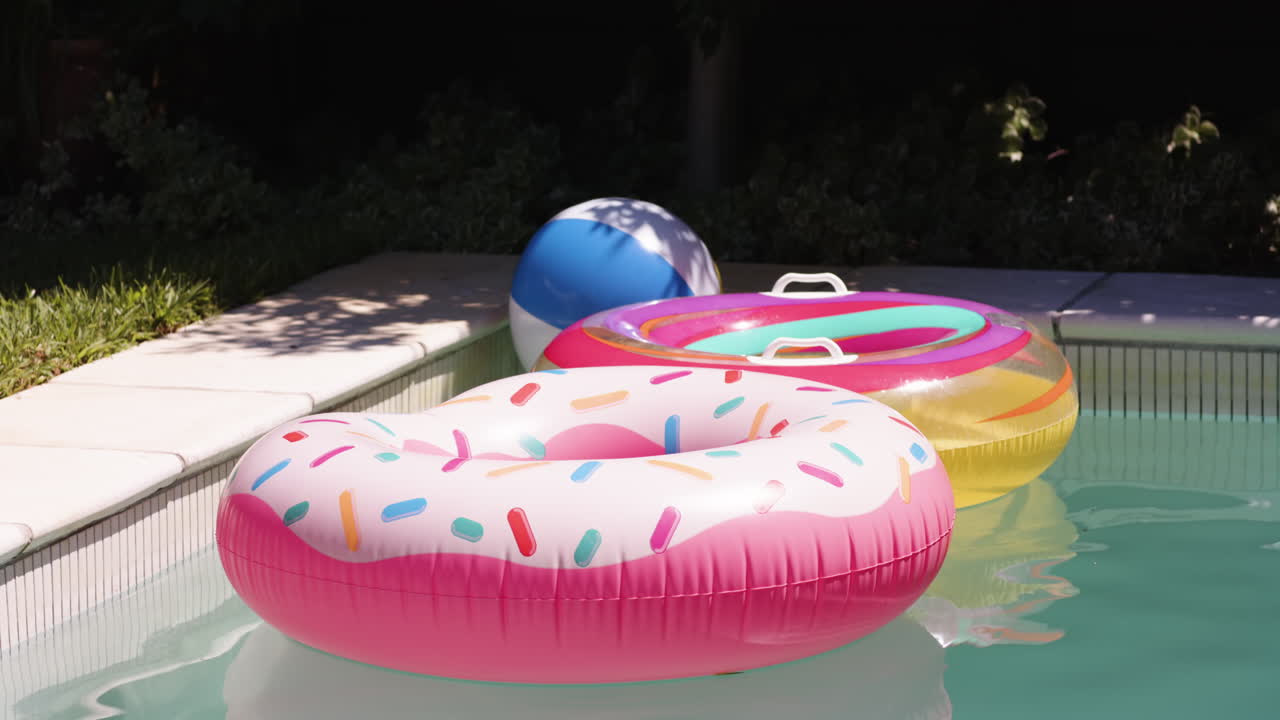 Colorful inflatable pool floats and beach ball floating in sunny backyard pool