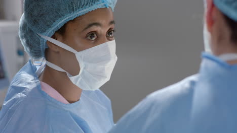 diverse female surgeons wearing surgical gowns discussing work in operating theatre, slow motion