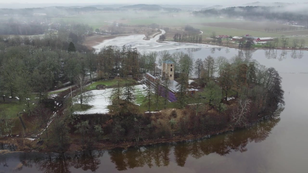 Veduta aerea di un parco di un castello storico su una penisola lacustre in un paesaggio di inizio primavera.