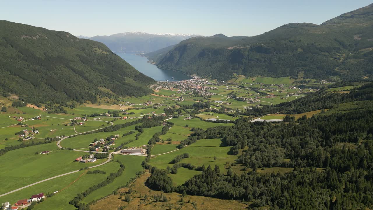 Cinematic 4K drone shot moving forward and sideways over Vik i Sogn in Vestland, Norway, revealing green fields, winding roads, cars, and fjord views under summer sunlight