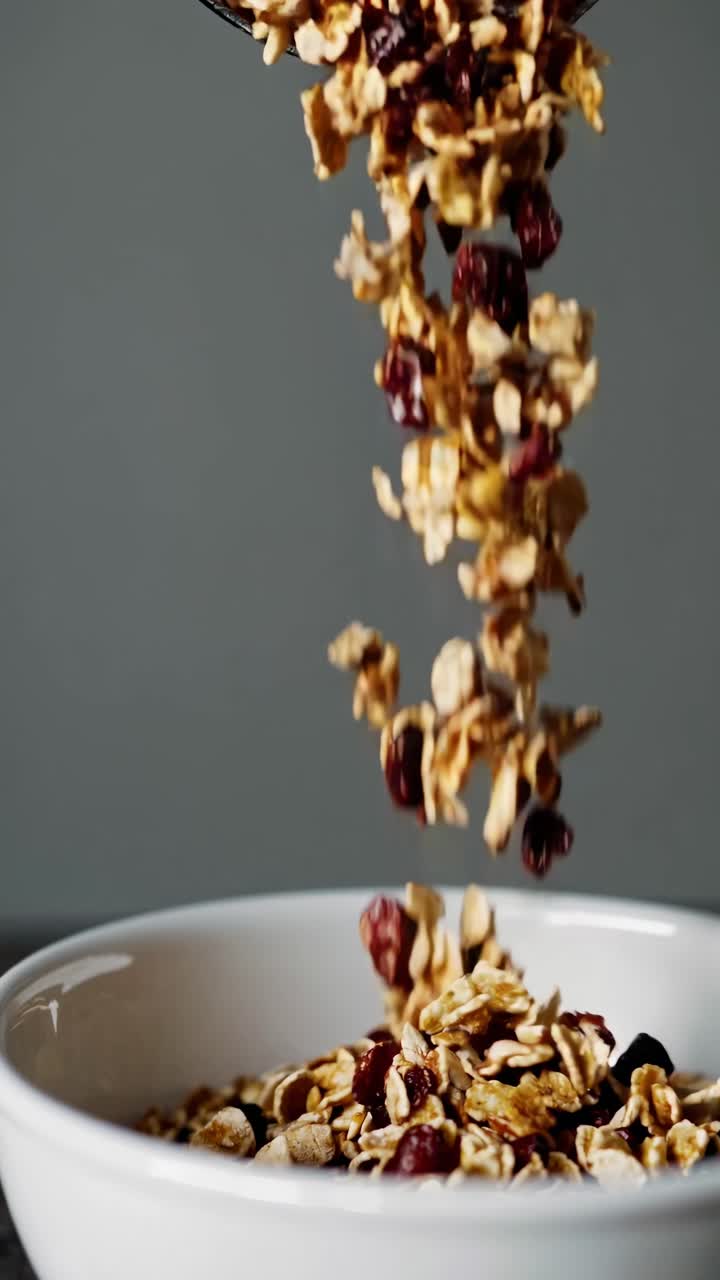 Close-up video shot of granola falling into a white bowl, captured from a side angle