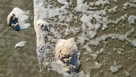 dirty ocean foam froth slowly moving across sandy welsh beach with tide waves