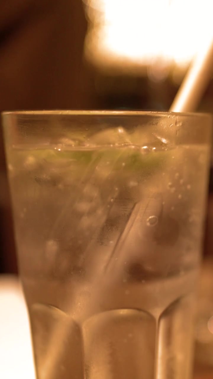Primo piano di una bevanda gassata fredda con cubetti di ghiaccio in un ristorante con luce soffusa.