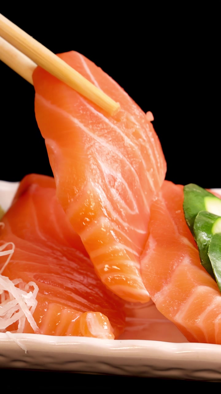 Essstäbchen nehmen Scheiben von Lachs-, Thunfisch- und Jakobsmuschel-Sashimi von einer kunstvoll angerichteten Sushi-Platte mit Rogen, Zitrone und Garnitur unter Studiobeleuchtung auf.