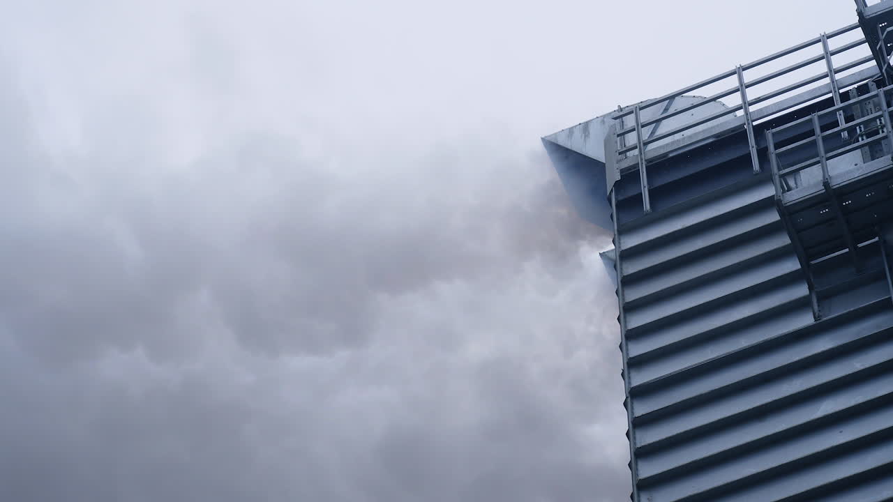 Clouds of grey thick smoke coming from the pipe in the industrial grain dryer. High metal building of industrial grain dryer at work.