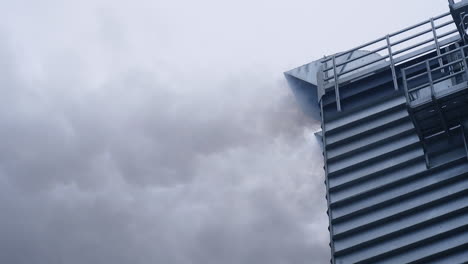 clouds of grey thick smoke coming from the pipe in the industrial grain dryer. high metal building of industrial grain dryer at work.
