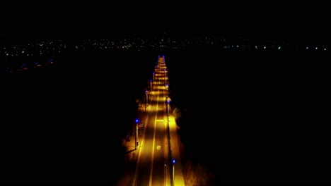 aerial night view of a glowing street lined with lights stretching toward a dark horizon