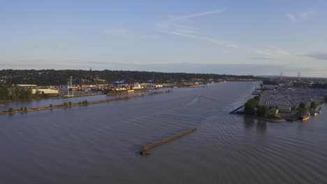 Río-Panorámico-Aéreo-Sobre-Pasaje-Industrial-Comercial-Para-Cargueros-De-Barcos-De-Carga-Para-Caminos-De-Importación-Y-Exportación-Hacia-El-Océano-Principal-Bifurcado-Entre-Casas-Residenciales-De-Lujo-De-Gran-Altura-Y-Transporte-Público