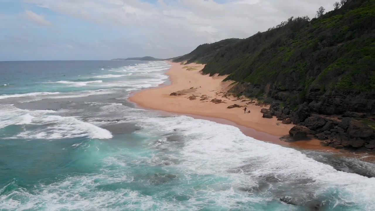 Ampia panoramica aerea dell'oceano su un'isola privata, con onde che si infrangono sugli scogli e persone che camminano sulla spiaggia.