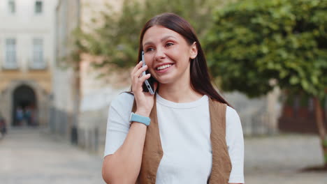 happy young caucasian woman in casual talking gossip on smartphone while walking on city street