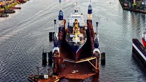 large cargo ship under repair in dry dock with cranes, aerial drone view