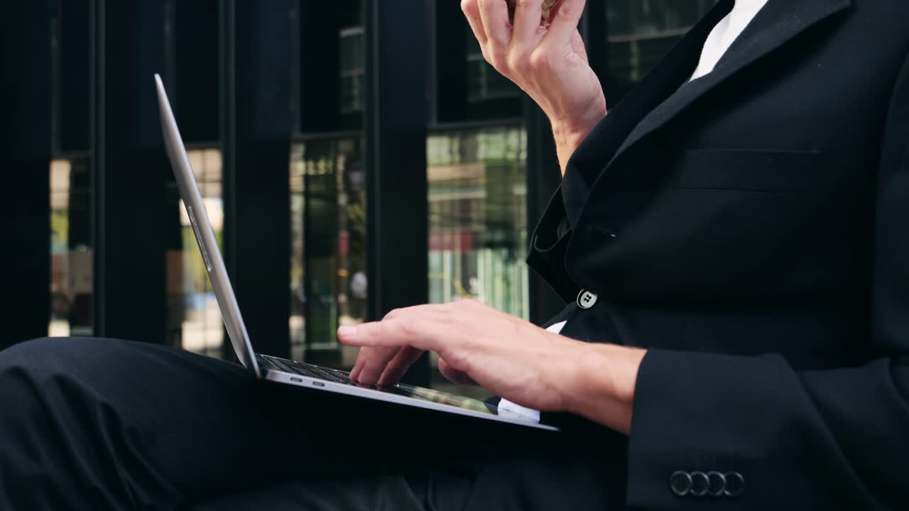 Man in suit working on laptop while eating a sandwich
