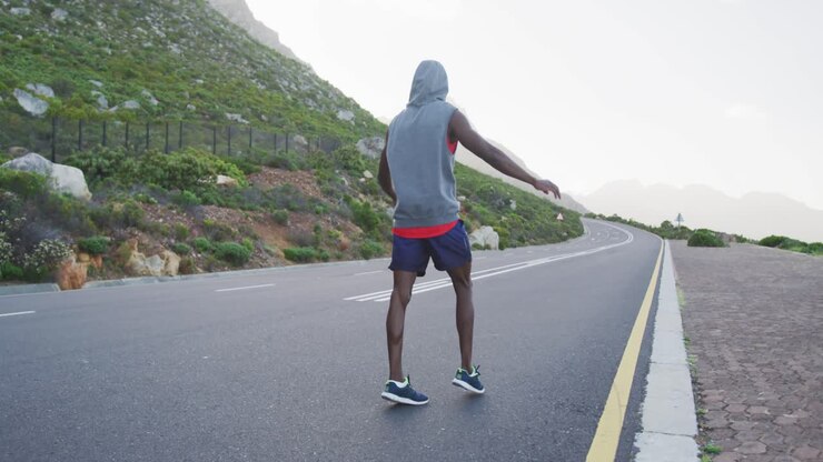 Uomo afroamericano con felpa con cappuccio che fa stretching e corre su strada