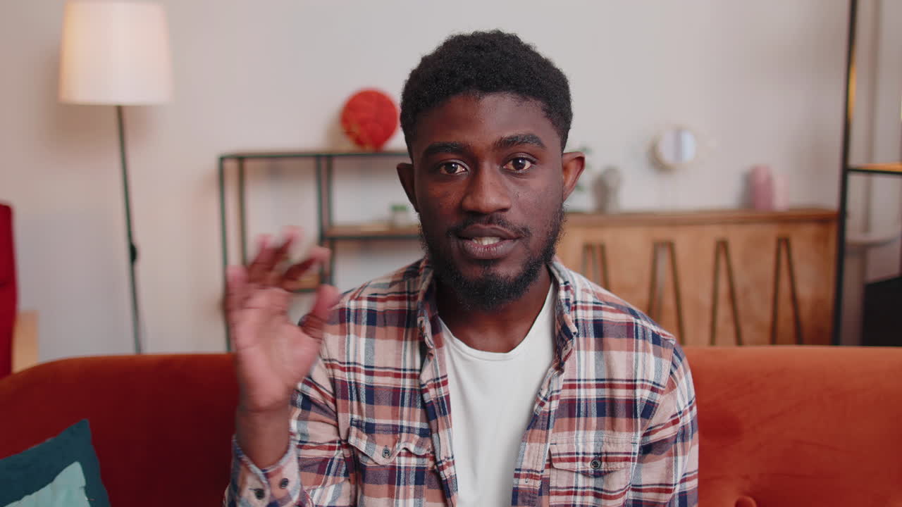 Man sitting on home sofa, looking at camera, making video conference call with friends or parents