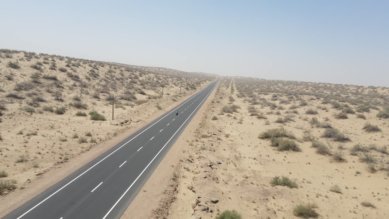 Aerial drone shot showcasing the vastness of the desert as a lone bike cruises down the center of the road.