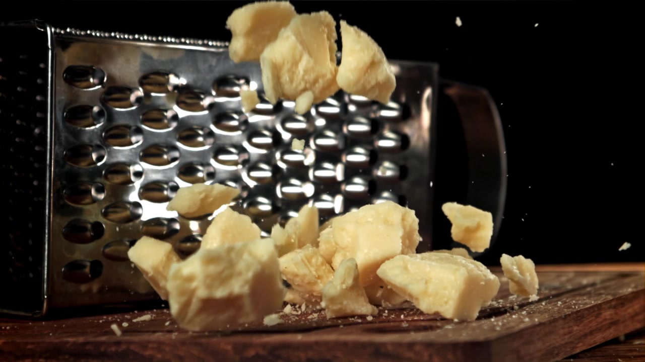 Pezzi di Parmigiano Reggiano che cadono su un tagliere di legno