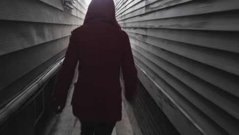 분홍색 보닛과 빨간 재킷을 입은 젊은 여성이 좁은 골목에서 누군가로부터 도망치고 있습니다.