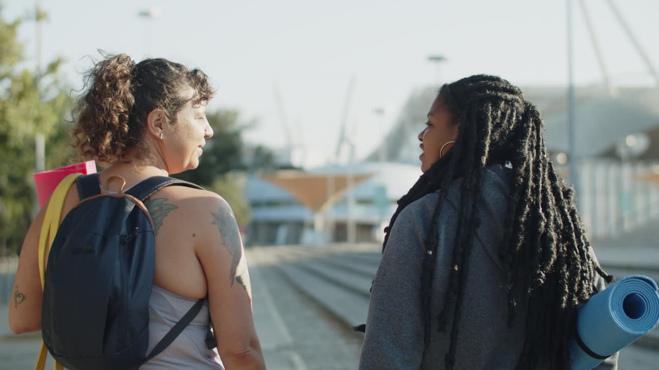 vista posterior de mujeres con esteras de ejercicio que van al parque para entrenar