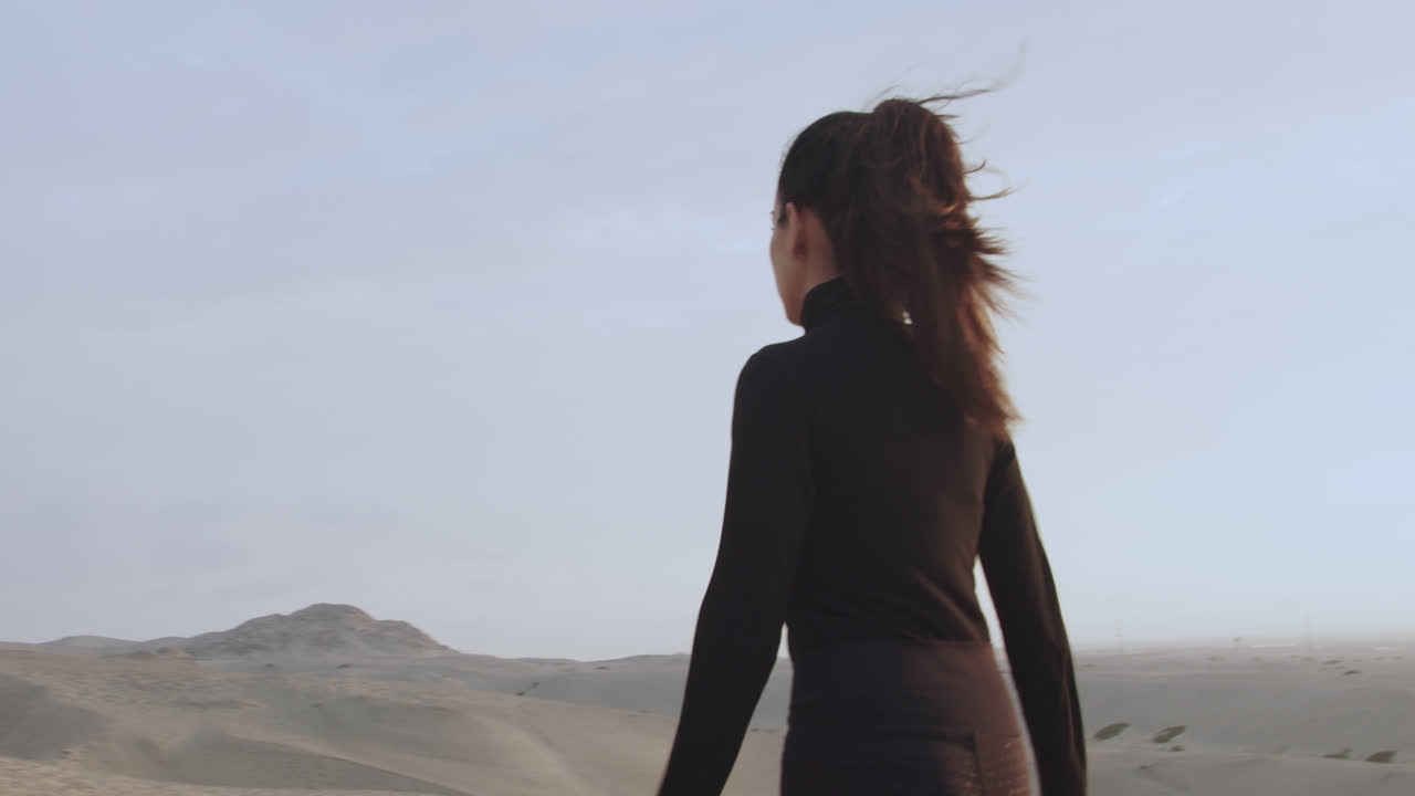 Slow motion medium shot of a beautiful and mysterious woman seen in profile while walking in a desert at sunset against the sunlight