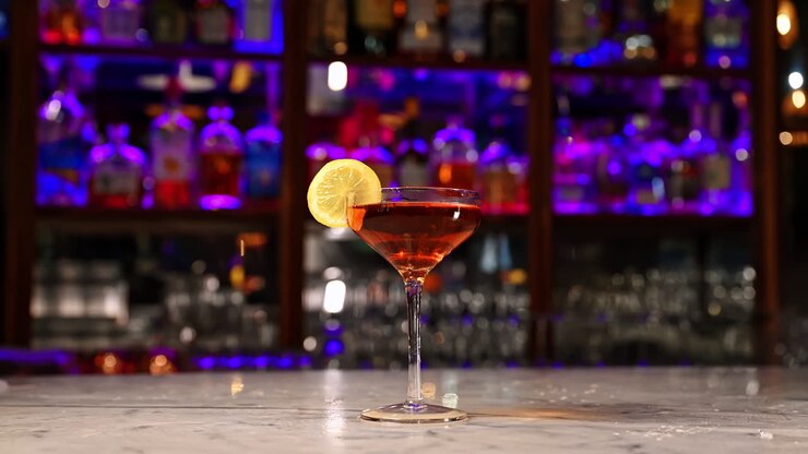 Cocktail ambrato con guarnizione di limone sotto le luci del bar. Elegante coppa di cocktail ambrato con guarnizione di limone, posizionata su un bancone di marmo in un bar illuminato al neon.