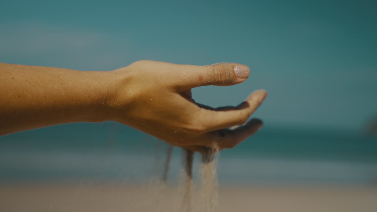mano de mujer vertiendo arena en verano en la playa