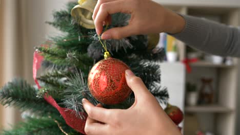 woman decorating christmas holiday tree at home with red balls, close