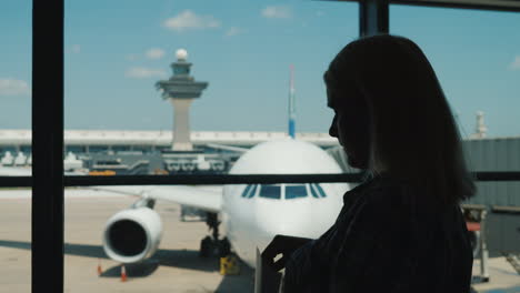 Silueta-De-Una-Mujer-En-La-Ventana-De-Una-Terminal-Del-Aeropuerto-Comiendo-Bocadillos-Mientras-Espera-Un-Vuelo