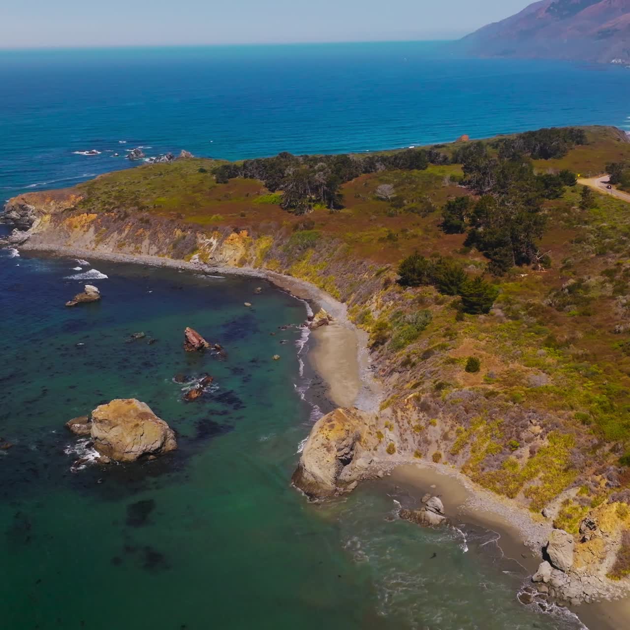 Beautiful rocky shore of the ocean with scarce vegetation. Calm ocean waters at mountainous coastline of Morro Bay, California, USA. Aerial view