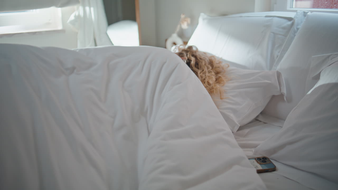 Sleeping woman reading mobile phone message. Awake calm girl turning alarm clock