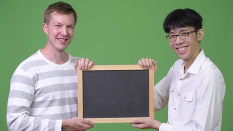 two happy young multi-ethnic businessmen holding blackboard together