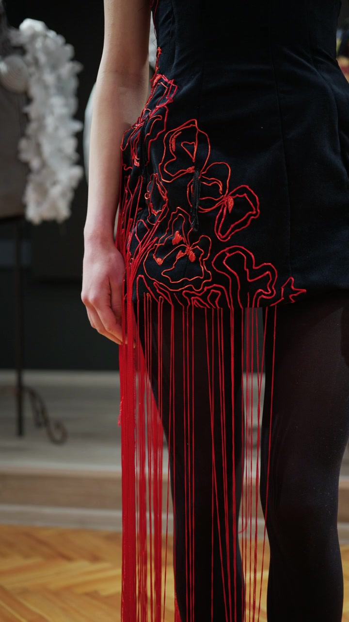 Primo piano di una modella che indossa un abito nero con elementi di filo rosso che si estendono verso l'esterno, creando una tensione lineare attraverso il corpo
